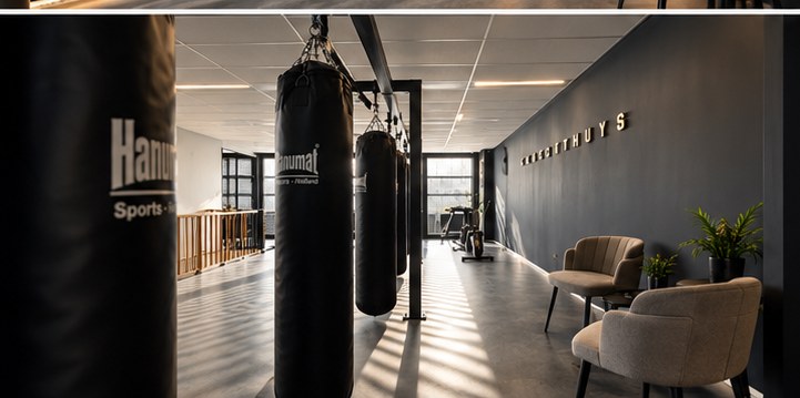 Doorkijk langs bokszakken richting trainingsapparatuur